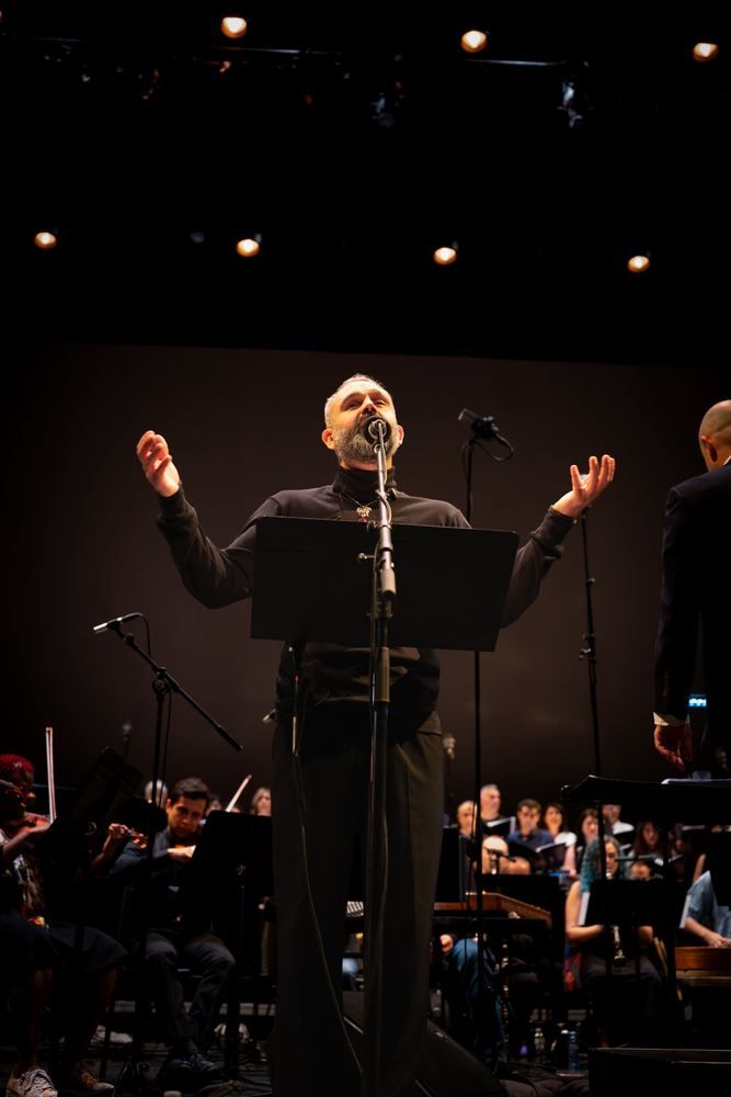 Milad Bagheri singing with arms open before orchestra and choir